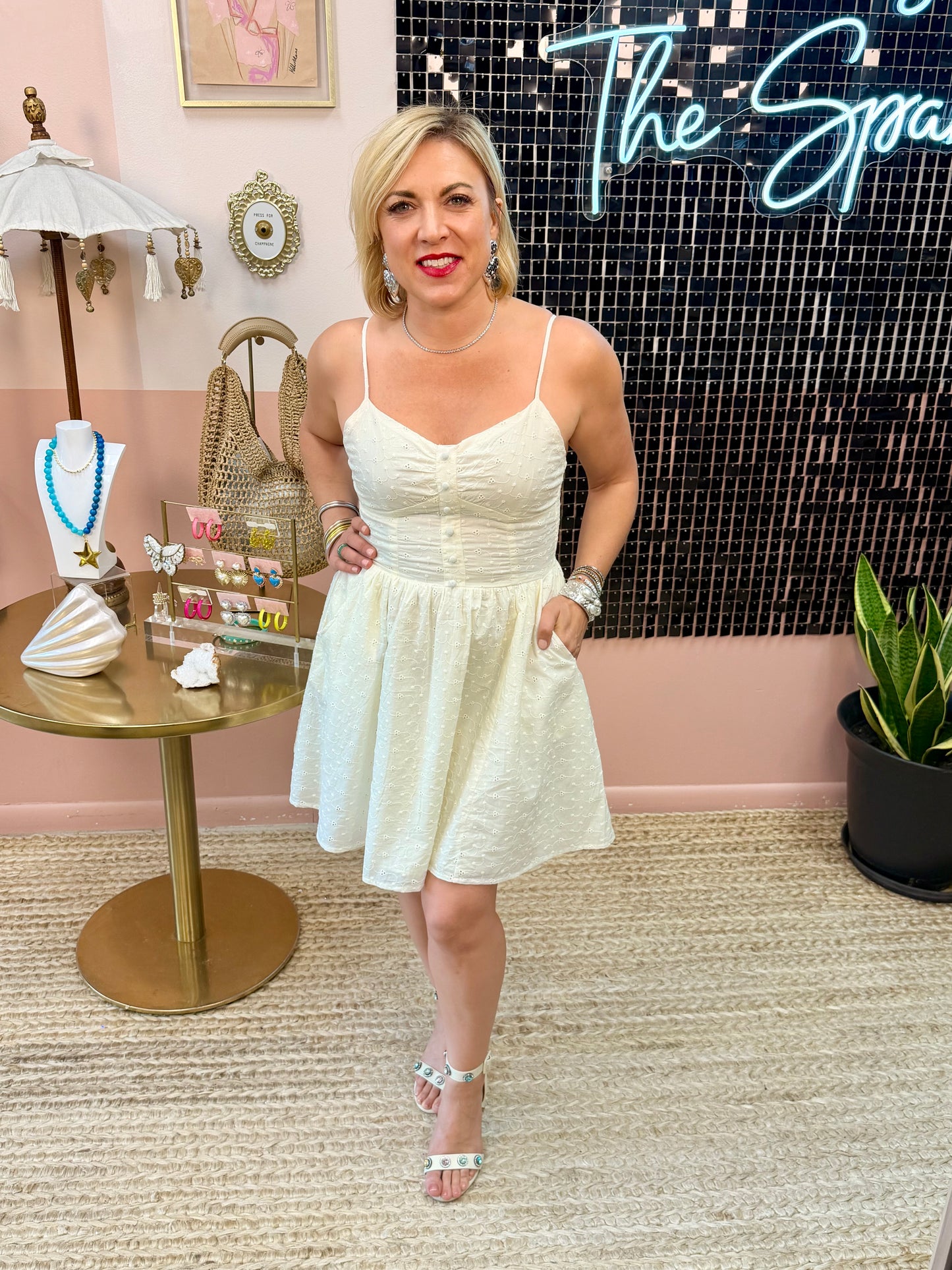 Woman in a white dress standing in a decorated room with a table and plants.