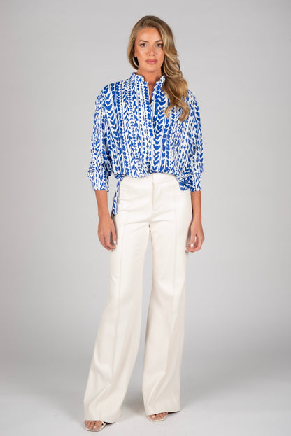 Woman wearing a blue patterned blouse and white pants on a gray background